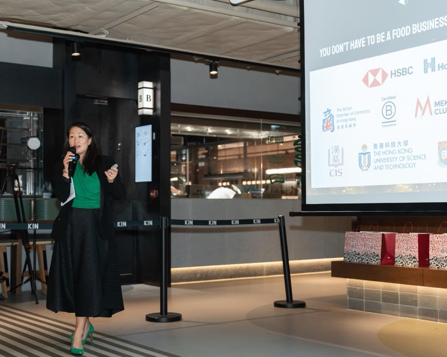 Heidi Spurrell presenting on stage at a Future Green event, with client logos on the screen behind her